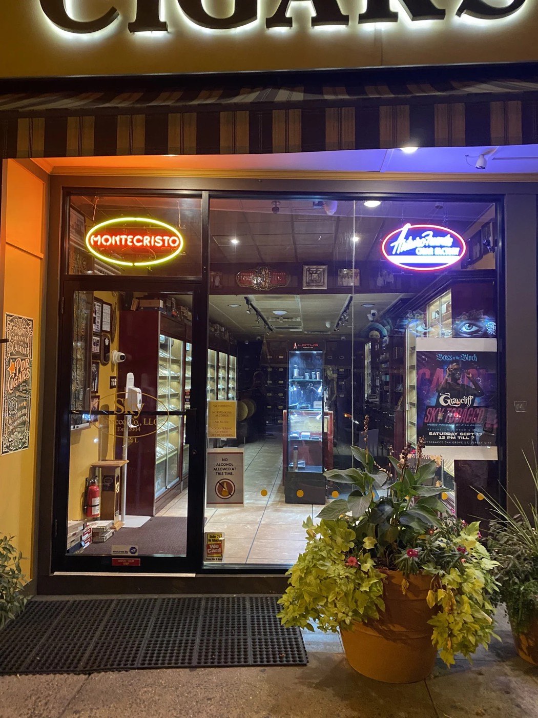 Sky Tobacco Company: storefront at night, lit cigars sign and neon. Photo from their website.